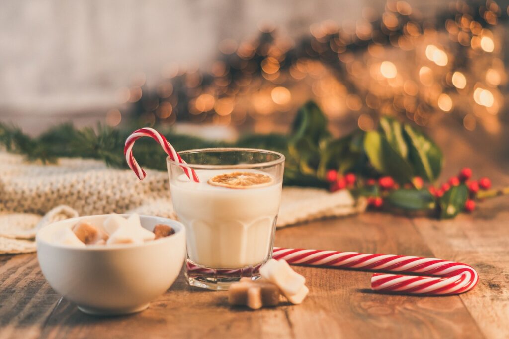 eggnog and a candy cane in front of a tree| holiday cocktails